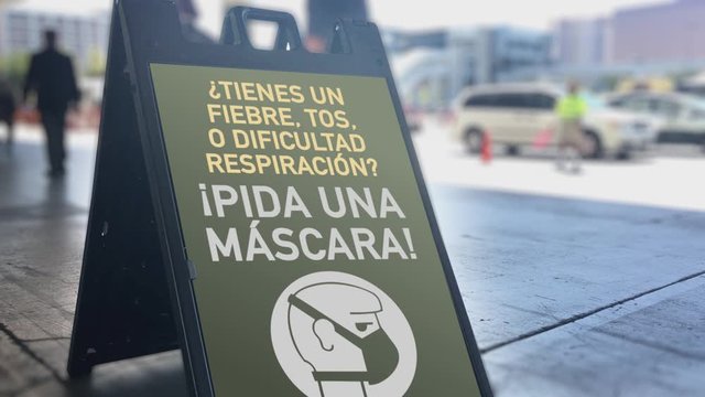 A Spanish sign in a busy city area informs pedestrians to ask for a face mask to help the spread of Coronavirus COVID-19. English version available.	