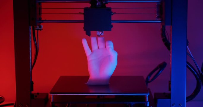 3D printer prints model hands fingers ok sign made white plastic closeup red blue neon light. Clear movements of print head and printer working platform. Potential modern 3D printing technology