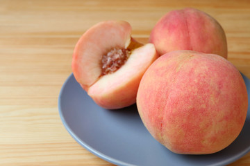 Fototapeta na wymiar Closeup Fresh Ripe Peaches on Blue Plate with Blurry Cut Peach in the Backdrop