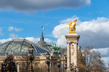 Fototapeta na wymiar Golden statue and lanterns of Pont Alexandre III bridge with Grand Palais and French flag waving on top of the building - Paris, France