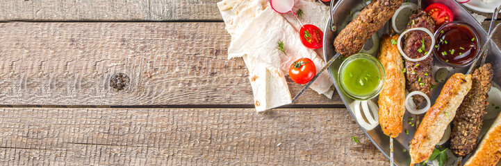 Summer bbq party. Shish kebab on a stick, from ground beef and chicken meat. Lula kebab, traditional Caucasian asian dish. With various sauces, spices and tomatoes, grey stone background