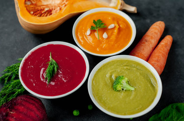 Set of vegetable soups. Broccoli, spinach, green peas soup. Pumpkin and carrot soup. Beetroot and carrot soup on a stone background.