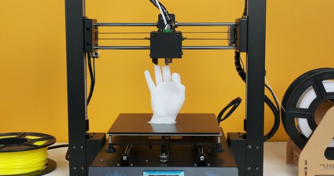 3D printer prints model hands made of white plastic close-up on yellow background. Clear movements of print head printer working platform. Modern 3D printing technology. Plastic spools of thread