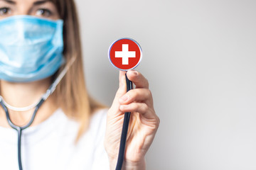 female doctor in a medical mask holds a stethoscope on a light background. Added flag of...
