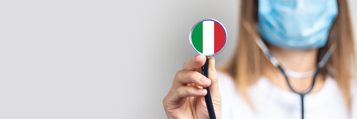 female doctor in a medical mask holds a stethoscope on a light background. Added flag of Italy....