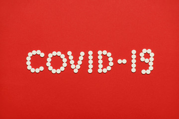 Top above overhead close up view photo of inscription of coronavirus covid-19 made of white round pills isolated over bright red background