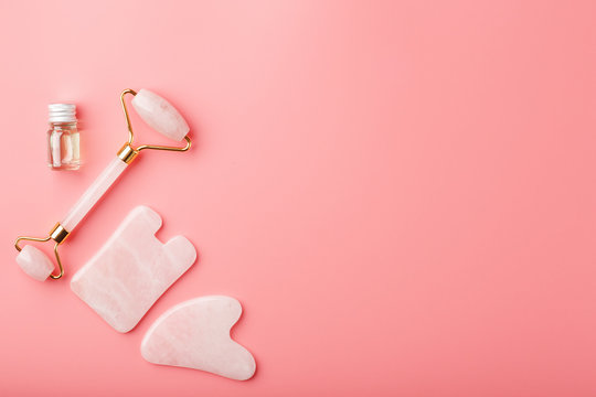 Gua sha massage tool made of natural pink Quartz-roller, jade stone and oil, on a pink background for face and body care. Part of traditional Chinese medicine