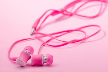 In-ear headphones on pink background, selective focus