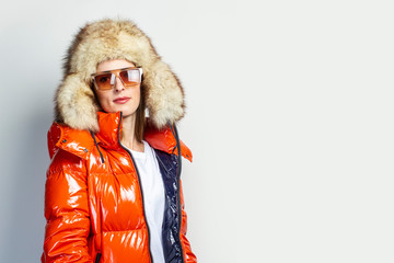 self portrait of a happy young girl in a red jacket and a fur hat on a light background. Fashion...