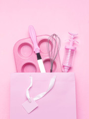 Kitchen accessories cupcake mold, whisk, spatula, cooking syringe in a pink bag on a pink background. Monochrome.