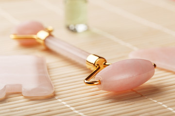 Gua sha massage made of natural rose Quartz-roller, jade stone and oil, on a bamboo background for face and body care.