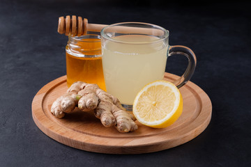 Ginger tea with honey and lemon lying on wooden cutting board  on black stone background. Virus...