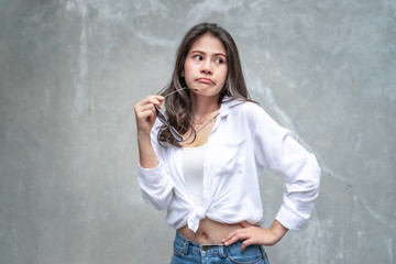 Asian beautiful woman with yellow skin, long black hair, wearing a white shirt, jeans showing her emotions.  Cement wall background