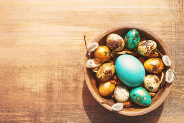 Bright easter eggs in a clay bowl and fluffy willow branches on a old wooden background, top view. Easter background.	