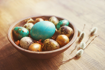 Bright easter eggs in a clay bowl and fluffy willow branches on a old wooden background, soft focus.	