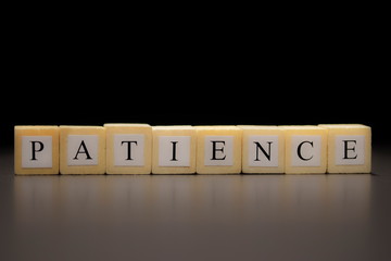 The word PATIENCE written on wooden cubes, isolated on a black background...