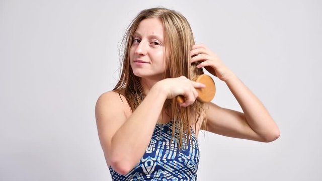 Beautiful woman is brushing her wet hair with wooden hairbrush