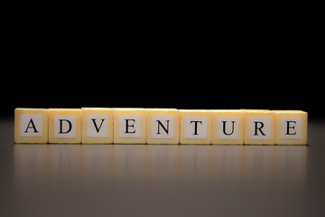 The word ADVENTURE written on wooden cubes, isolated on a black background...