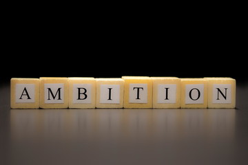 The word AMBITION written on wooden cubes, isolated on a black background...