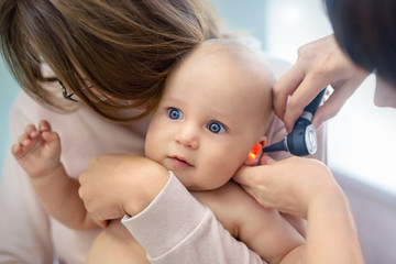 Doctor pediatrist examining childs ear with otoscope. Mom holding baby with hands. Medicine,...