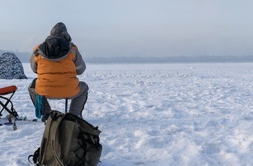 Fototapeta na wymiar fisherman in winter fishing sitting on a chair on the ice of the lake against the background of a tent
