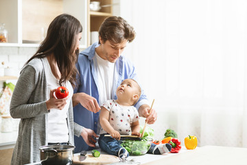 Happy parents teaching baby son to prepare vegetable salad