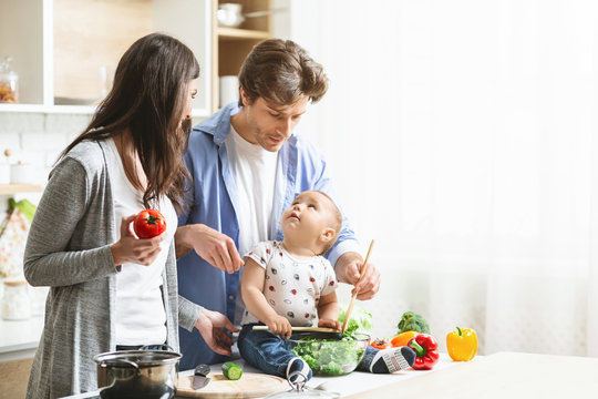 Happy Parents Teaching Baby Son To Prepare Vegetable Salad