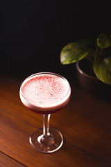 Raspberry smoothie with foam and berry crumbs in a glass on a wooden table in a dark bar.