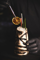 Tiki Drink Cocktail on the bar. Bartender with gloves decorates the drink with dried orange.