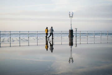 Dos personas corriendo junto al mar y reflejados en el agua en Gijón