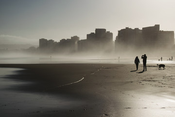 Edificios altos frente a la playa en una mañana de niebla y gente caminando