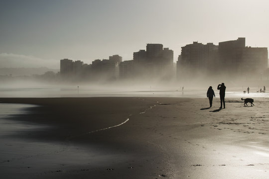 Edificios altos frente a la playa en una ma&ntilde;ana de niebla y gente caminando