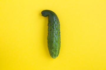Ugly food. Ugly cucumber in the center of the yellow background. Top view. Copy space.