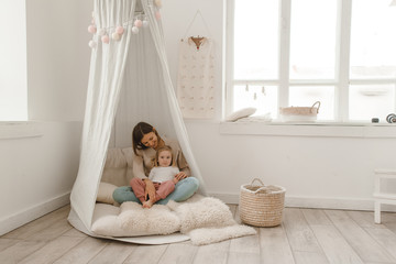 Cute baby girl with her mom play in a minimalistic children's room.