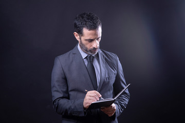 Uomo vestito in abito, segna degli appunti in un agenda - Isolato su sfondo nero