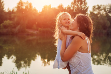 Mother's day. Woman playing having fun with daughter by summer river at sunset. Woman holding kid...