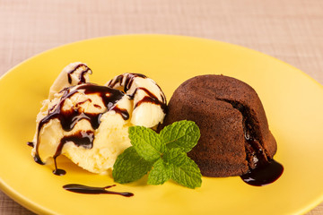 petit gateau with vanilla ice cream and a sprig of mint on yellow plate