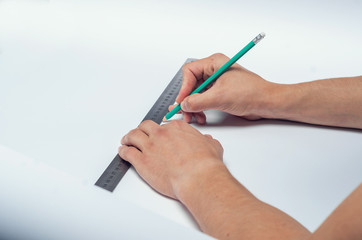 Male hand draws a pencil under a ruler on a white sheet of paper