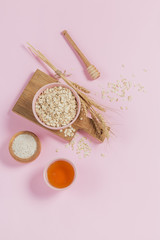 Bowl of dry oat flakes with honey, oatmeal and ears of wheat on light background. Healthy skin, facial and body care.