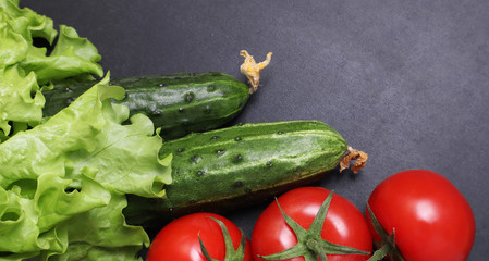 Green lettuce, red ripe tomatoes on a branch, fresh cucumbers and red bell peppers paprika. Vegetables on a black textured background.