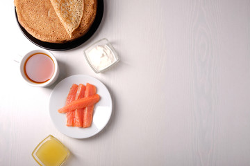 Plate with pancakes on a white table, honey, sour cream, red fish, top view