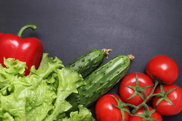 Green lettuce, red ripe tomatoes on a branch, fresh cucumbers and red bell peppers paprika. Vegetables on a black textured background.