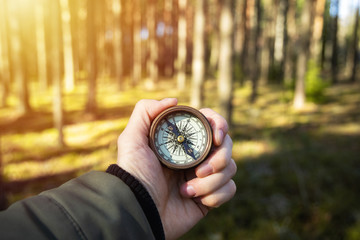 Compass in a hand with blurred trees background. Hiker searching direction with a compass in the...