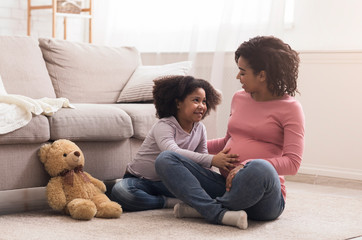 Adorable little black girl tenderly touching her mommy's pregant belly