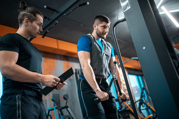 young man has workout with personal trainer in modern gym