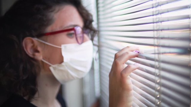 Woman wearing protective masks peeks through blinds