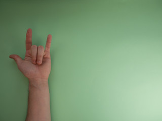 Female hand shows a gesture of rock horns on green background