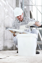 plasterer man at work, take the mortar from the bucket to plastering the wall of interior construction site wear helmet and protective gloves, and scaffolding on background