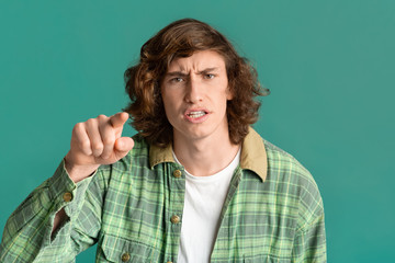 Frustrated teenager pointing finger at you in accusation on color background