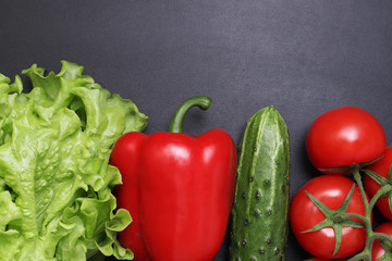 Green lettuce, red ripe tomatoes on a branch, fresh cucumbers and red bell peppers paprika. Vegetables on a black textured background.